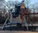 Outdoor space probe exhibit near the Prague Planetarium, displayed on metal supports beside the circular planetarium building, with trees and clear blue sky in the background.