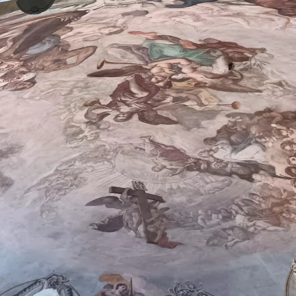 Ceiling fresco inside Saint Nicholas Church in Prague, showing dramatic Baroque religious scenes with angels, saints, and soft pastel tones painted across the curved dome.Ceiling fresco inside Saint Nicholas Church in Prague, showing dramatic Baroque religious scenes with angels, saints, and soft pastel tones painted across the curved dome.